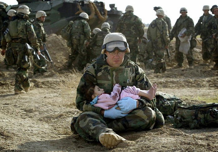 U.S. Navy Hospital Corpsman HM1 Richard Barnett, assigned to the 1st Marine Division, holds a child after she was separated from her family during a firefight [2003] Source: Damir Sagolj