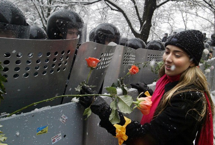 A Ukrainian woman places carnations into shields of anti-riot policemen standing outside the presidential office in Kiev. Ukraine, during the 2004 Orange Revolution. [2004] Source: Vasily Fedosenko